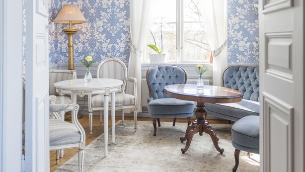 Une pièce comprenant une table à manger, des chaises, un canapé bleu, un lustre et un papier peint à motifs.