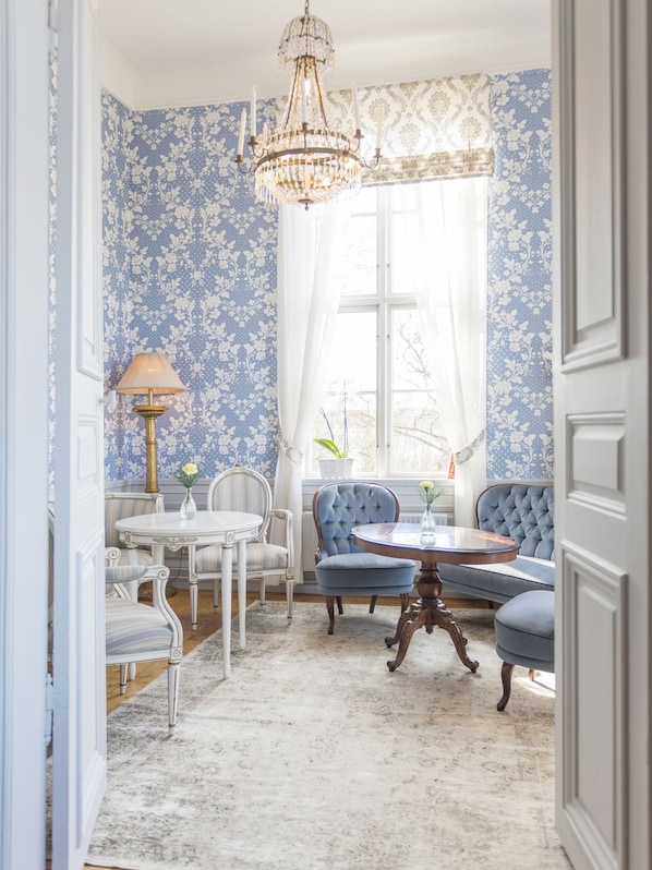 A room with a dining table, chairs, a blue sofa, a chandelier, and patterned wallpaper.