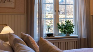 Une chambre avec une grande fenêtre, une lampe de chevet et une plante en pot posée sur le rebord de la fenêtre.