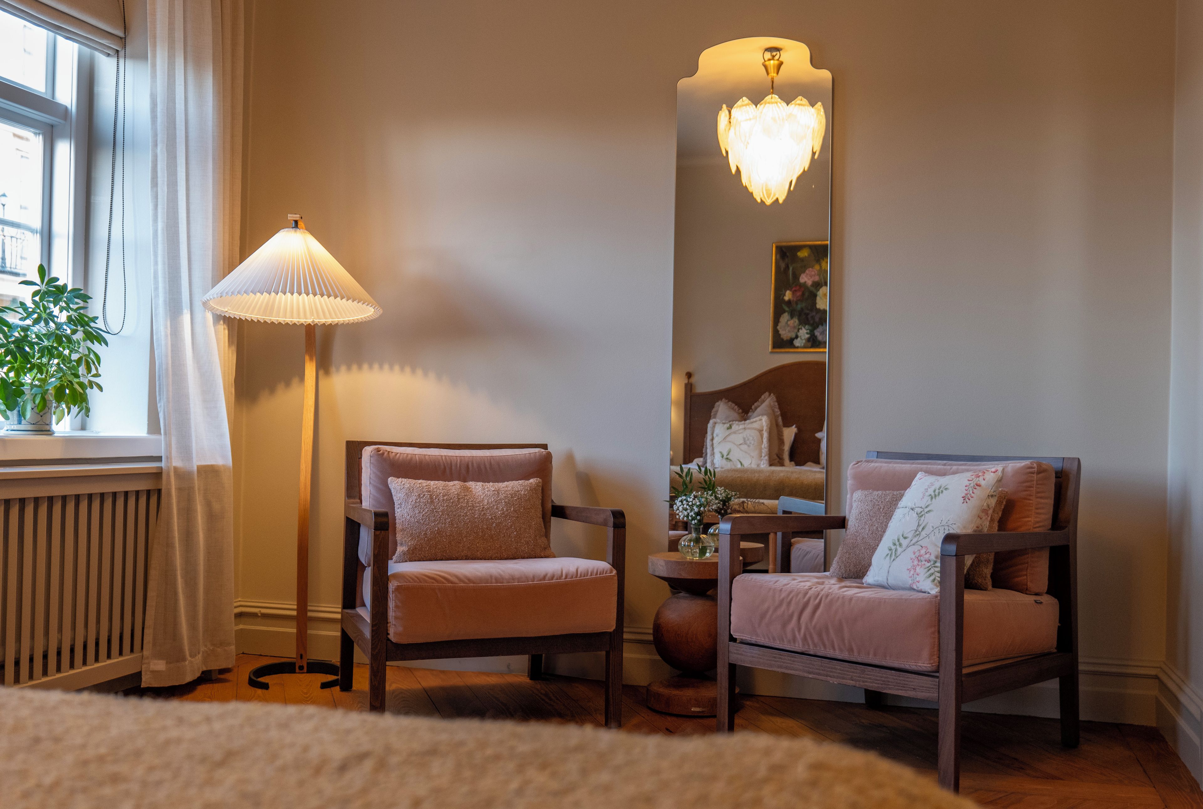 Una habitación con dos sillones, una lámpara de pie, un espejo y un radiador.