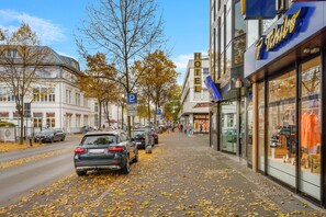A hotel with a modern facade, a visible parking sign, and a sidewalk lined with parked cars and fallen leaves. - Hotel Marktterrassen (Hennef)