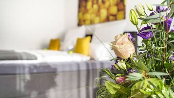 A bed with white bedding and a yellow pillow in a room with a painting on the wall.