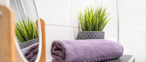 A bathroom with a mirror, a purple towel, and a potted plant.