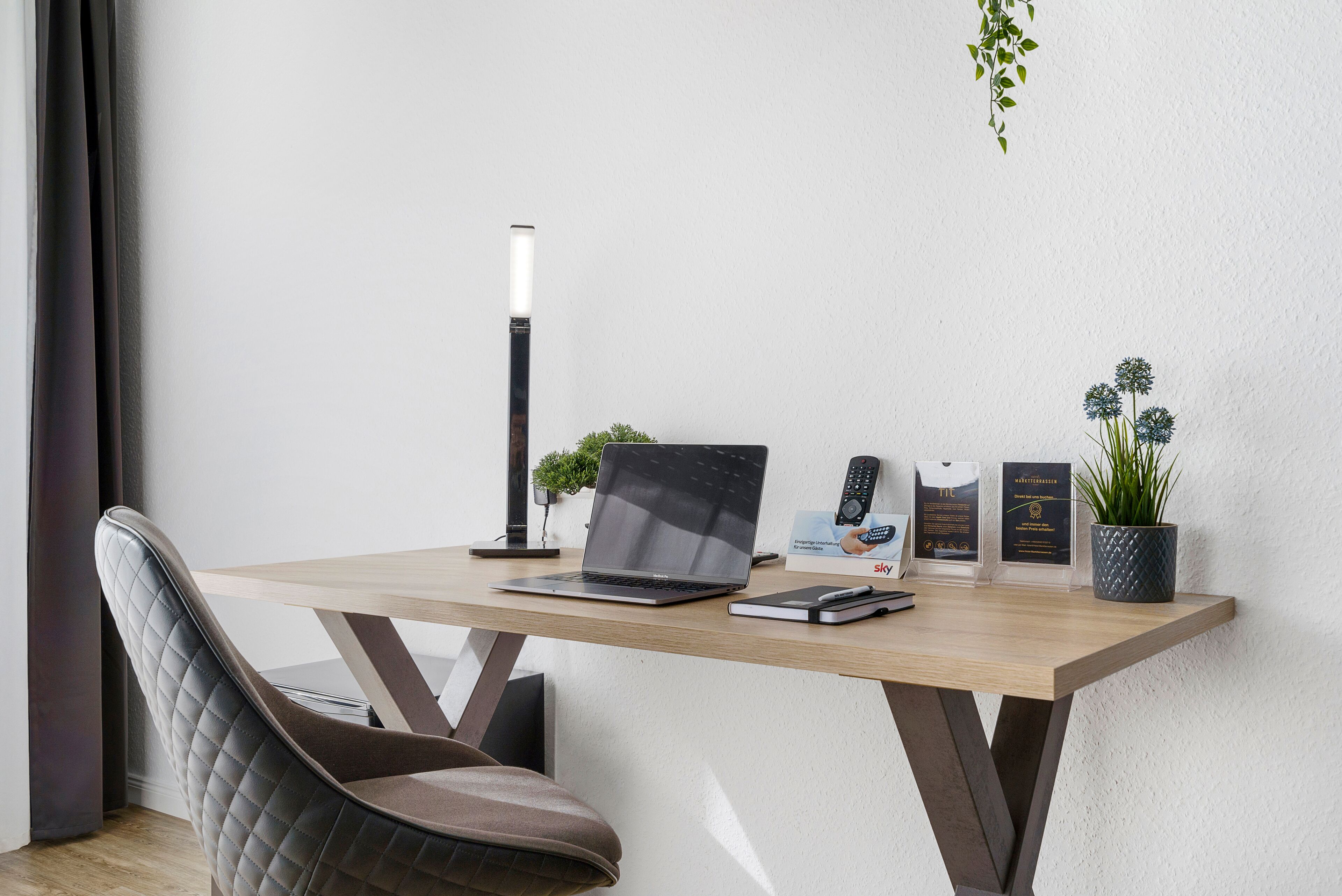 Un escritorio moderno con una computadora portátil, un teléfono inteligente, un control remoto y una planta.