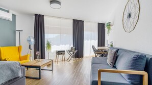 Una sala de estar moderna con un sofá, un sillón amarillo, una mesa de centro, una mesa de comedor con sillas y un ventanal con cortinas.
