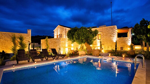 A swimming pool with lounge chairs and a stone building in the background. - Arcus Suites (Rethymno)
