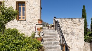 A stone staircase leading to a wooden door, surrounded by greenery and a clear blue sky. - Arcus Suites (Rethymno)