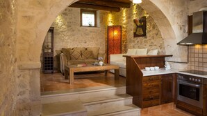A rustic stone-walled room with a wooden bench, a sofa, and a kitchen area with a stove. - Arcus Suites (Rethymno)