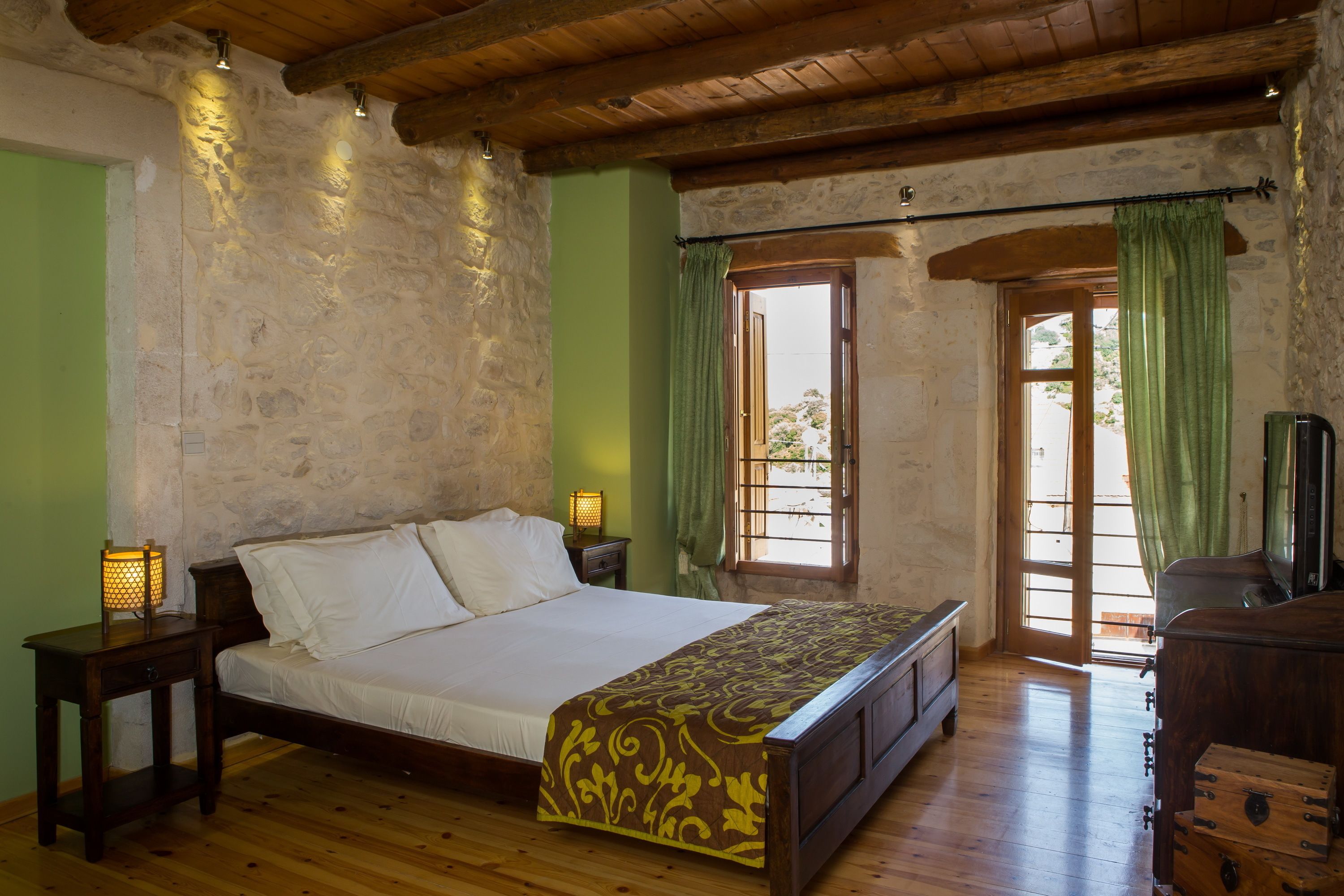 Une chambre à coucher avec un lit en bois, des murs en pierre, une porte verte et une commode en bois.
