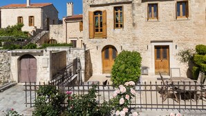A stone building with wooden shutters, a staircase, and a small garden with roses. - Arcus Suites (Rethymno)