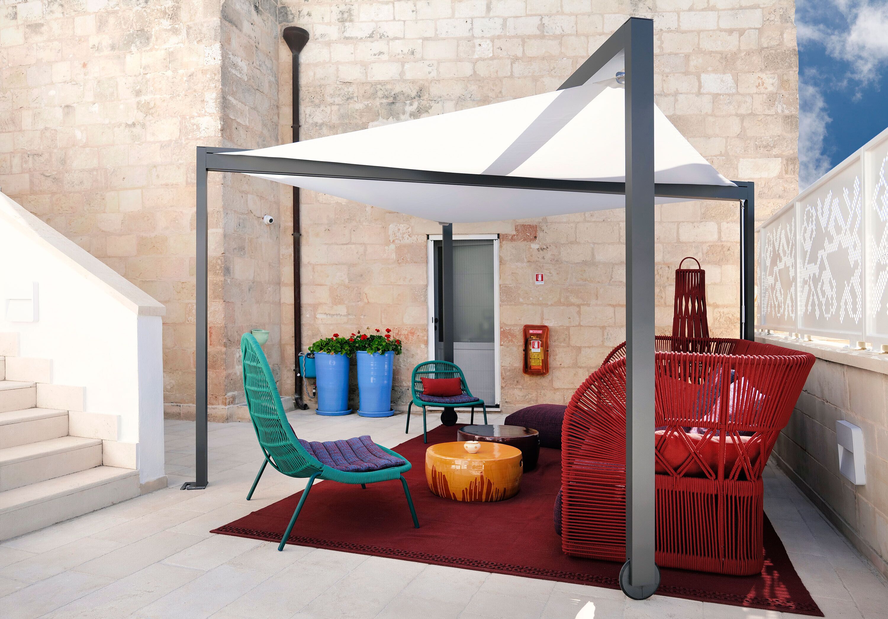 An outdoor seating area with a white canopy, a red chair, a green chair, and a round ottoman.