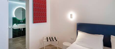 A modern hotel room with a bed, a bedside table, a small stool, a wall-mounted light, and a red patterned artwork.