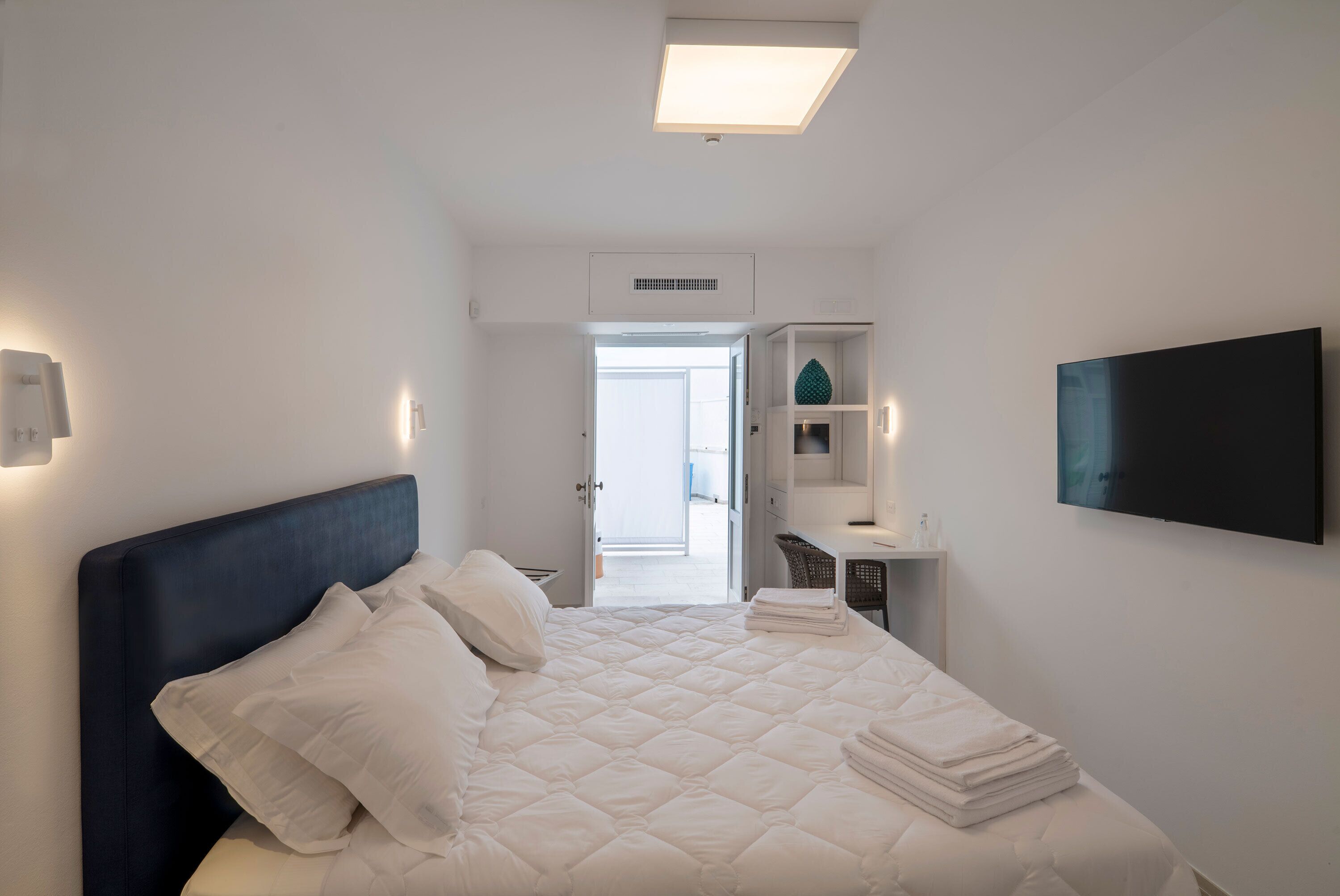 Une chambre d’hôtel équipée d’un lit, d’un bureau, d’une télévision et d’une porte donnant accès à une salle de bain.