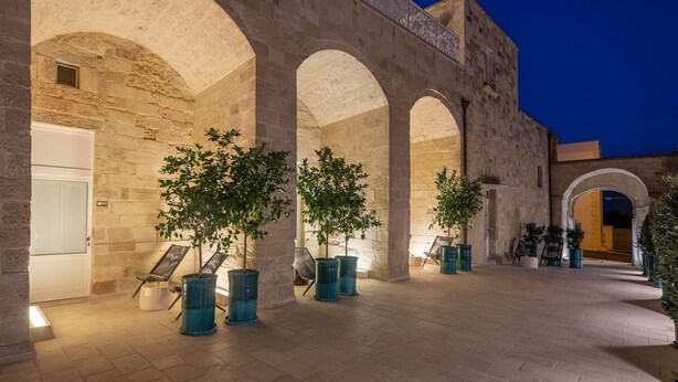 Un patio al aire libre con arcos de piedra, plantas en macetas y zonas de estar.