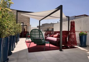 En tagterrasse med udendørs siddepladser, plantekasser og et hvidt markise.