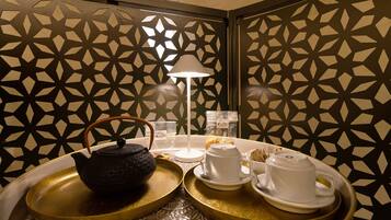 Une pièce dont un mur est décoré d’un motif géométrique, avec un plateau contenant un service à thé, une lampe blanche et une petite table sur laquelle sont posées des tasses et une théière.