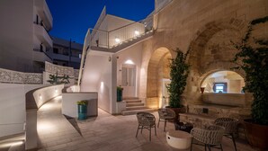 Un patio con un arco de piedra, mobiliario exterior y una escalera que lleva a un nivel superior.
