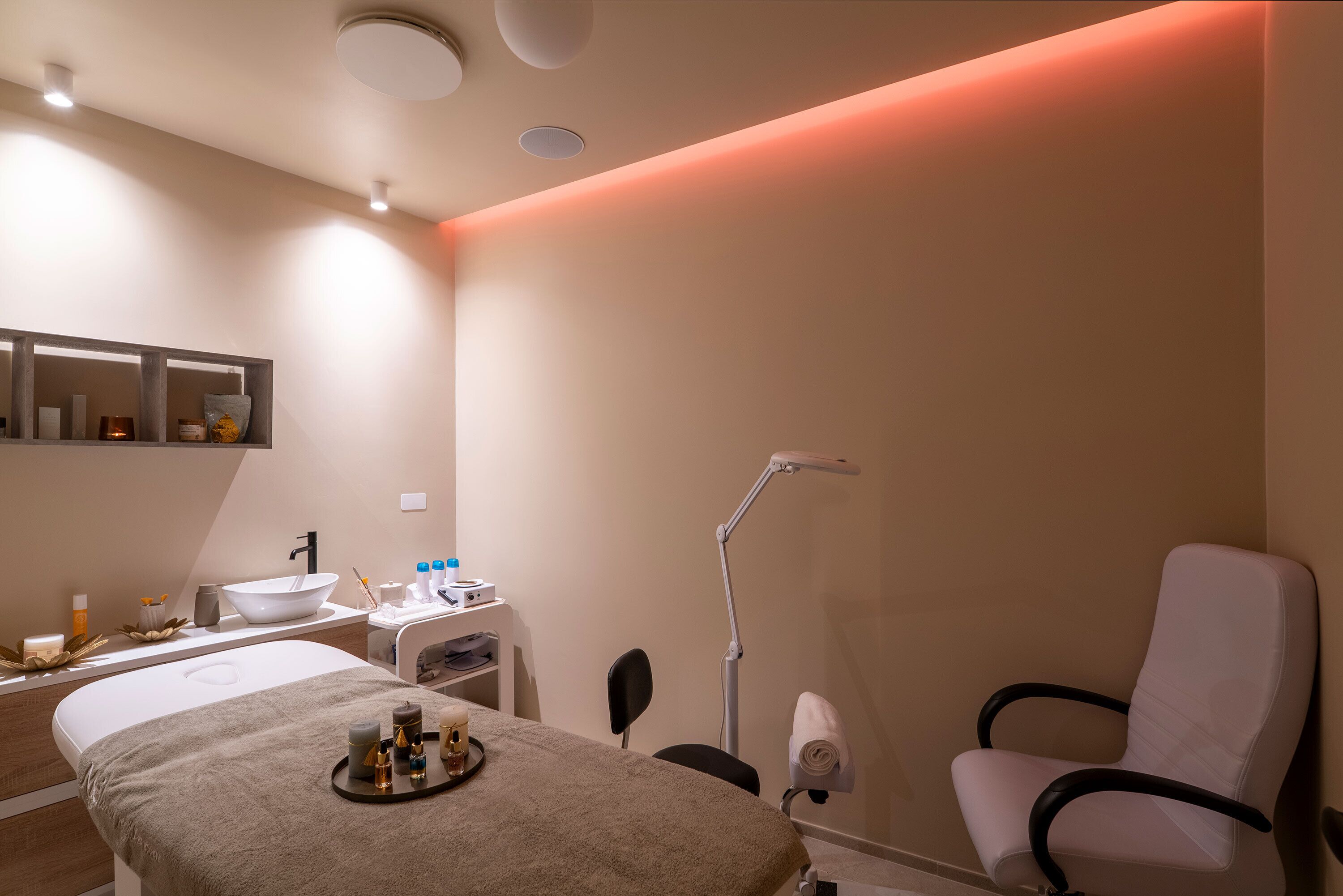 Ett modernt spa-rum med en massagebänk, en stol, ett handfat och en sminkbord med toalettartiklar.