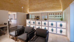 Zona de bar moderna con techo de ladrillo, barra blanca con adornos azules y asientos con cojines grises.