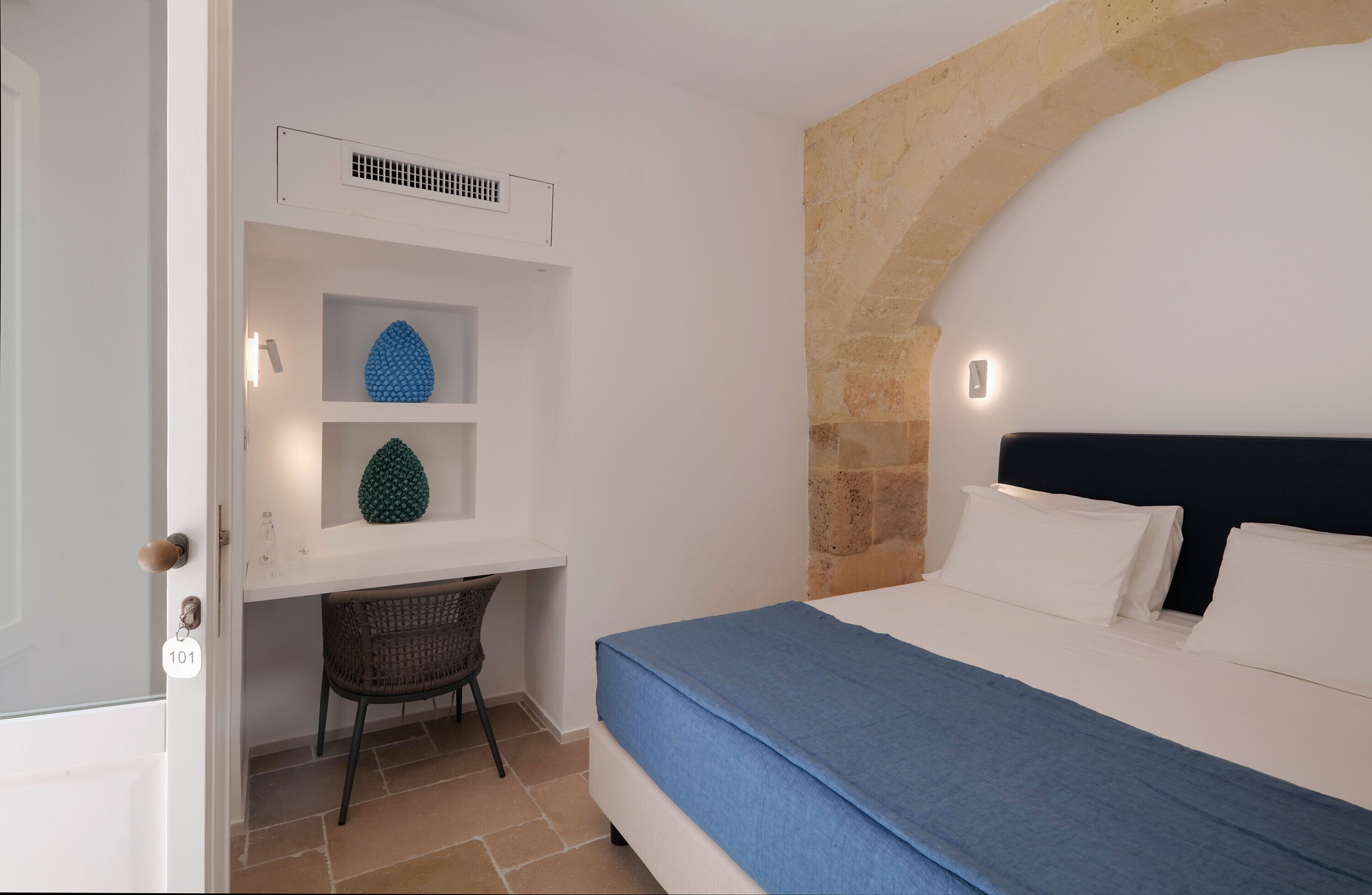 A bedroom with a bed, a desk with a chair, and a stone wall.