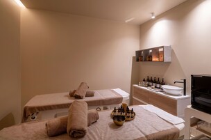 Un cuarto de spa con dos camillas de masaje, toallas, botellas de aceites y un lavamanos.
