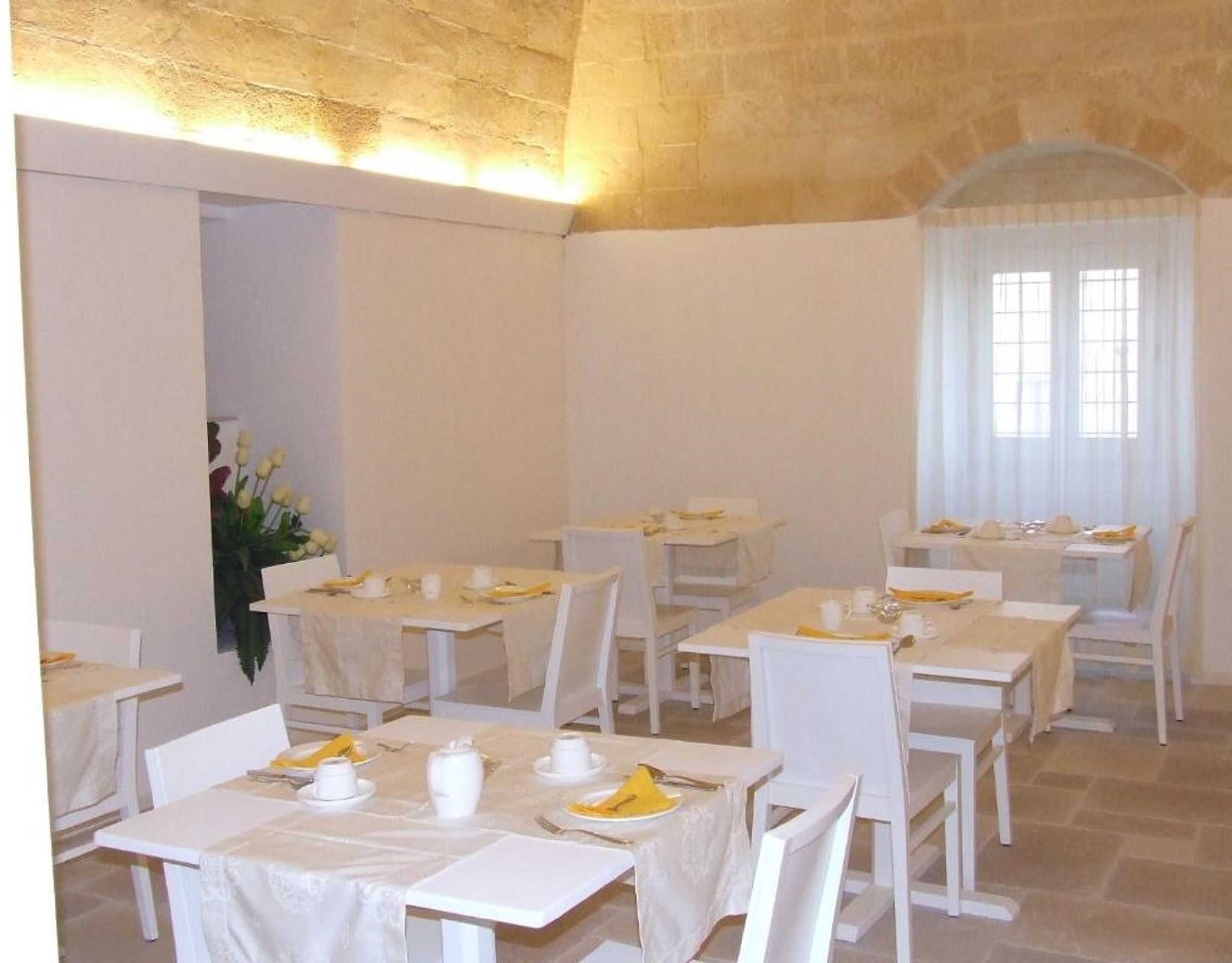 Un área de comedor con varias mesas y sillas, dispuestas en una habitación amplia con techo alto y paredes de piedra.