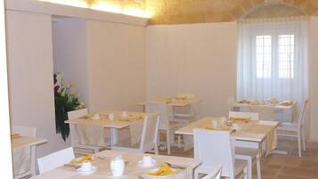 Un área de comedor con varias mesas y sillas, dispuestas en una habitación amplia con techo alto y paredes de piedra.