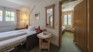 A hotel room with two beds, a small table, a mirror, and a view of another room through an open door.