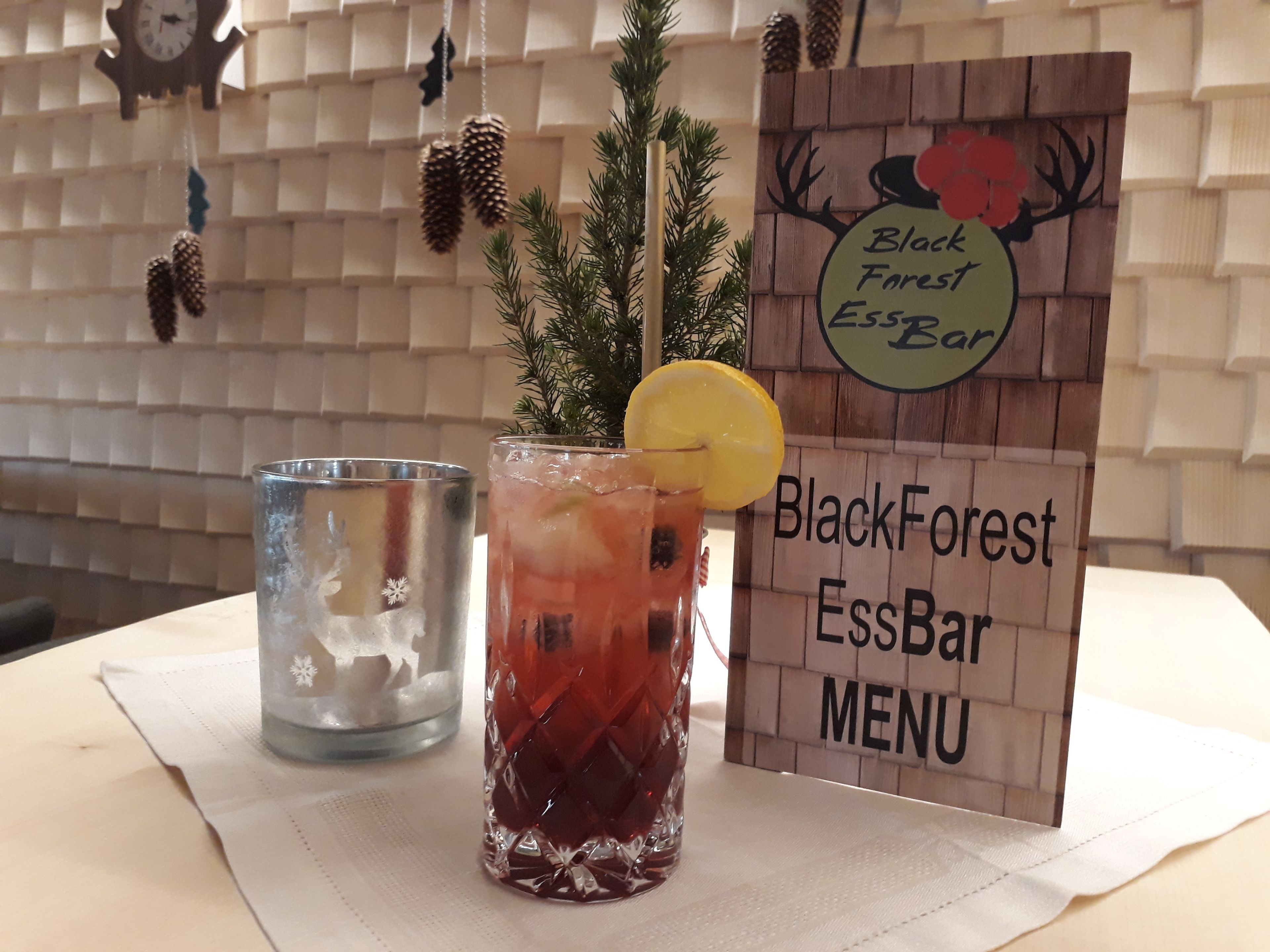 A menu board for BlackForest EssBar, a glass of iced tea with a lemon slice, and a glass of water on a table.