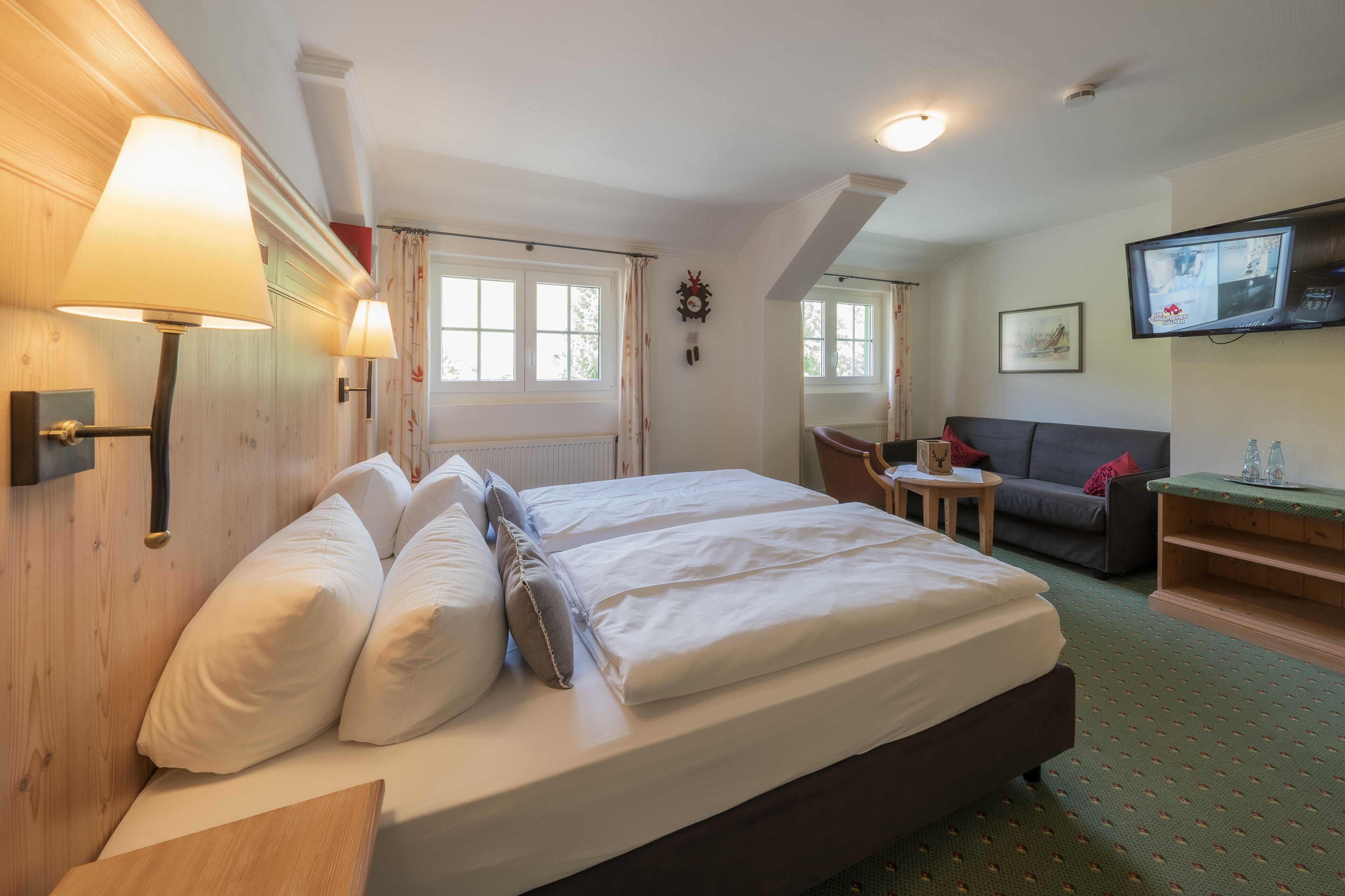 A hotel room with a large bed, a small table, a sofa, and a television.