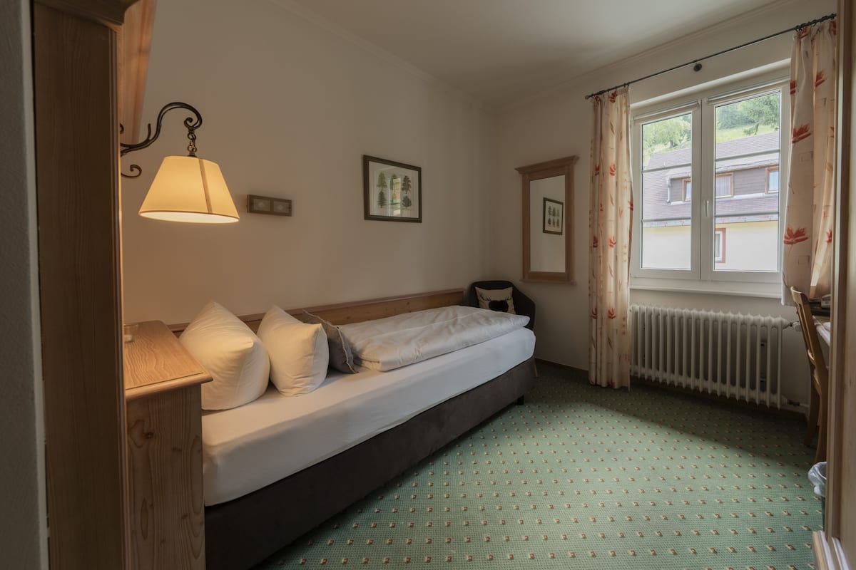 Un dormitorio con cama, una mesita de noche, una lámpara, una ventana con cortinas y un radiador.