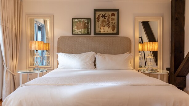 A large bed with white linens, two bedside tables with lamps, and framed botanical artwork on the wall. - The Lofts Boutique Hotel (Knysna)