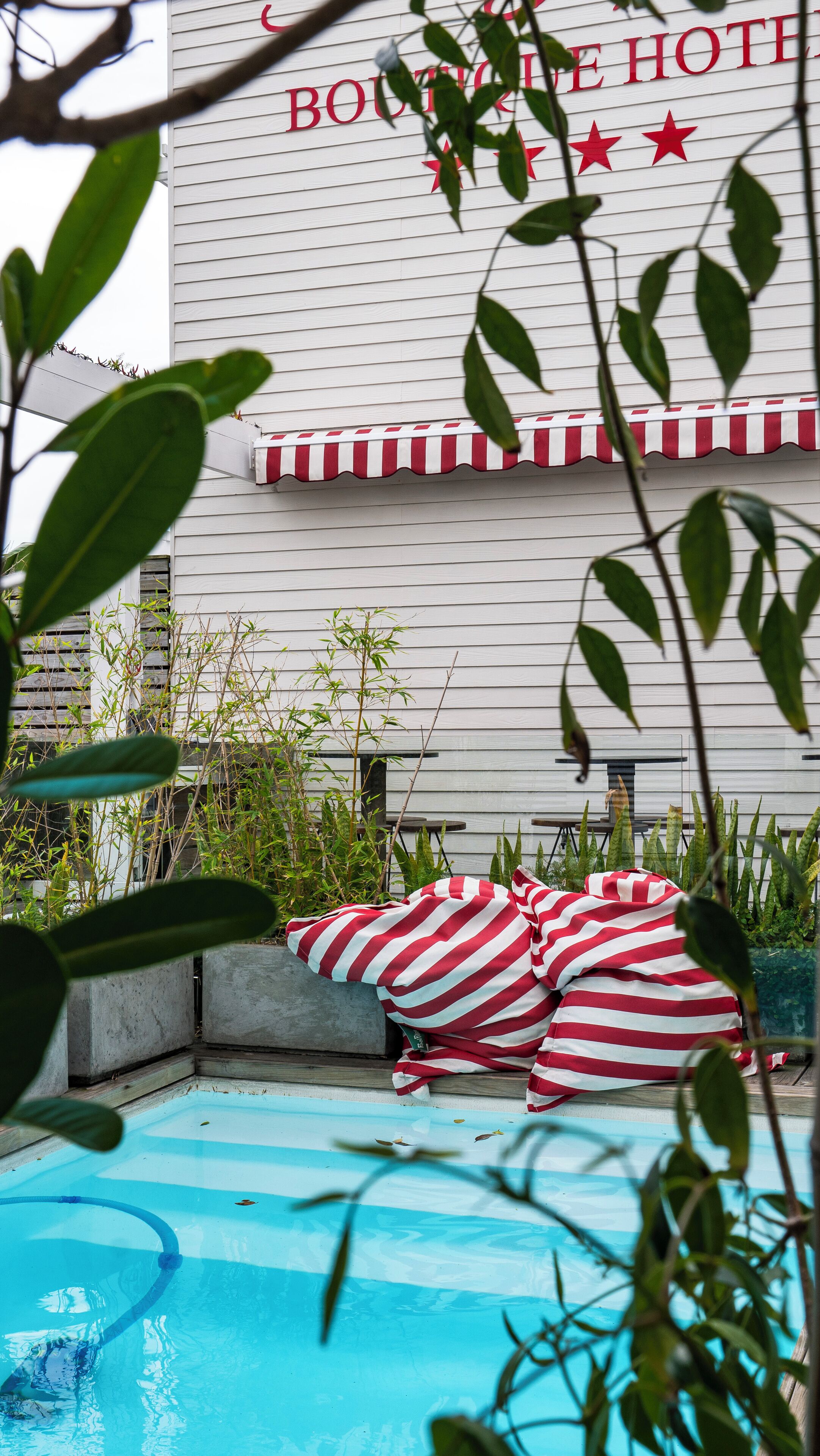 A pool area with striped cushions, a sign for Boutique Hotel, and surrounding greenery.