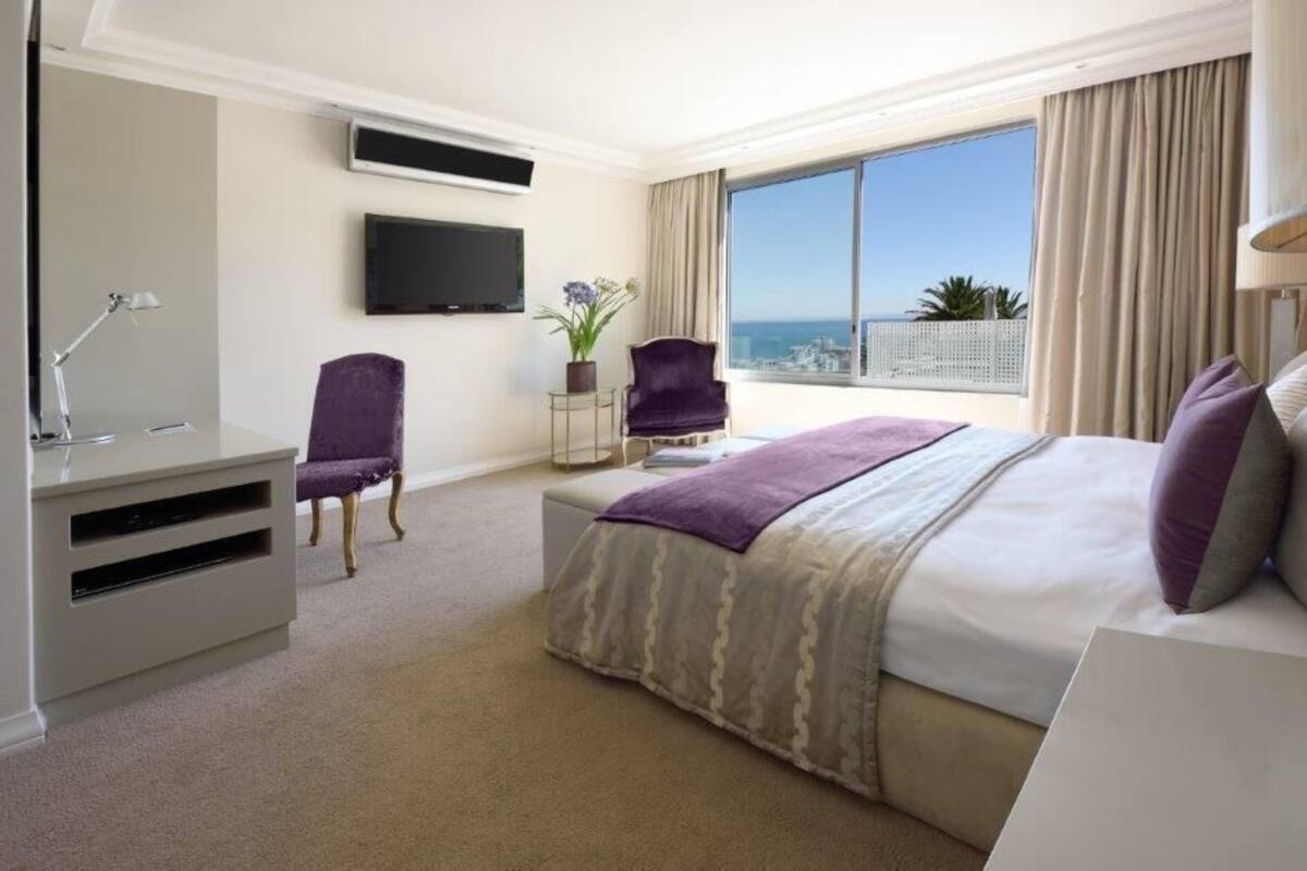 A hotel room with a bed, a desk, a chair, a TV, and a large window with a view.