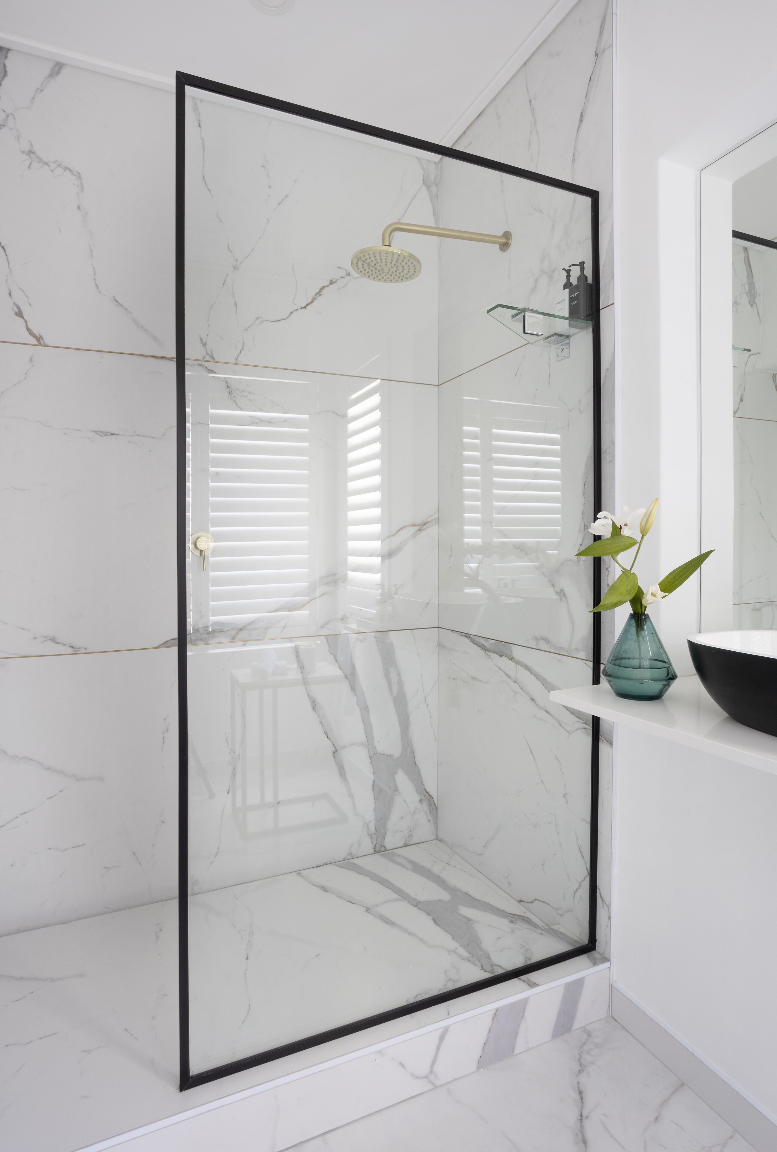Un baño moderno con ducha de vidrio, paredes de mármol y un florero sobre la encimera.