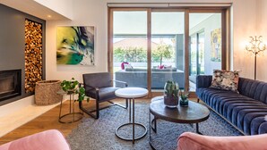 A modern living room with a fireplace, a sofa, a coffee table, and a large window offering a view of the outdoors. - The Clarendon - Fresnaye (Cape Town)