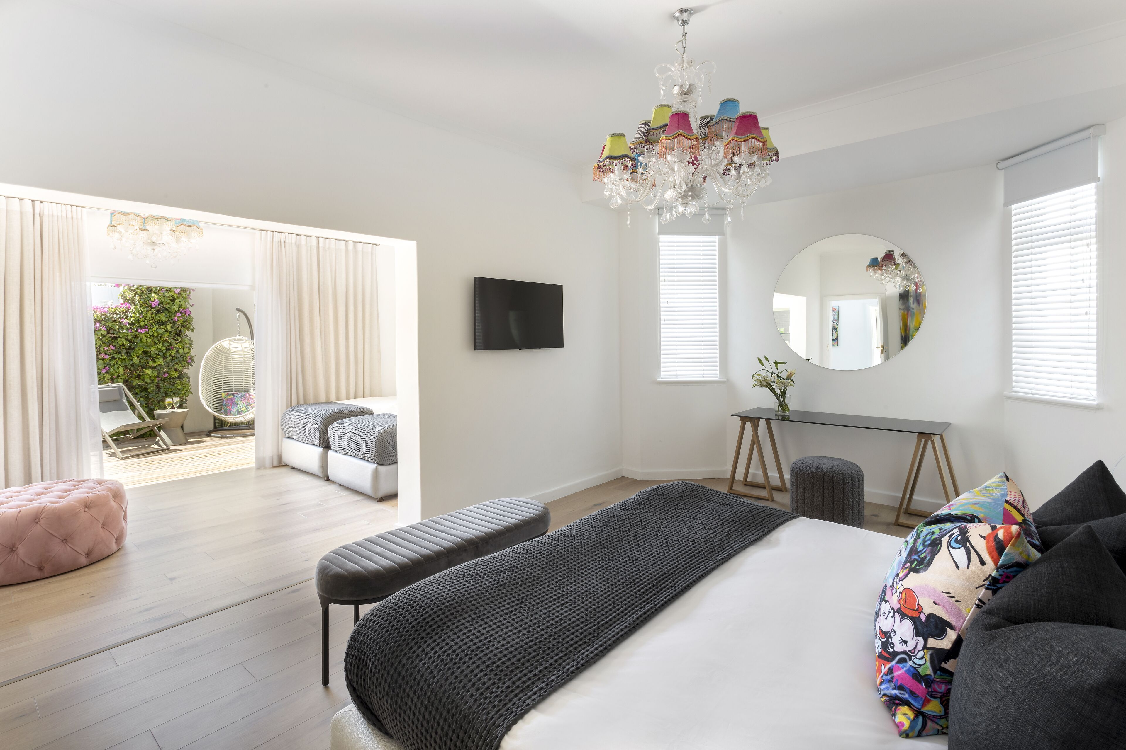 A modern bedroom with a large bed, a chandelier, a TV, and a balcony with a view of the outdoors.