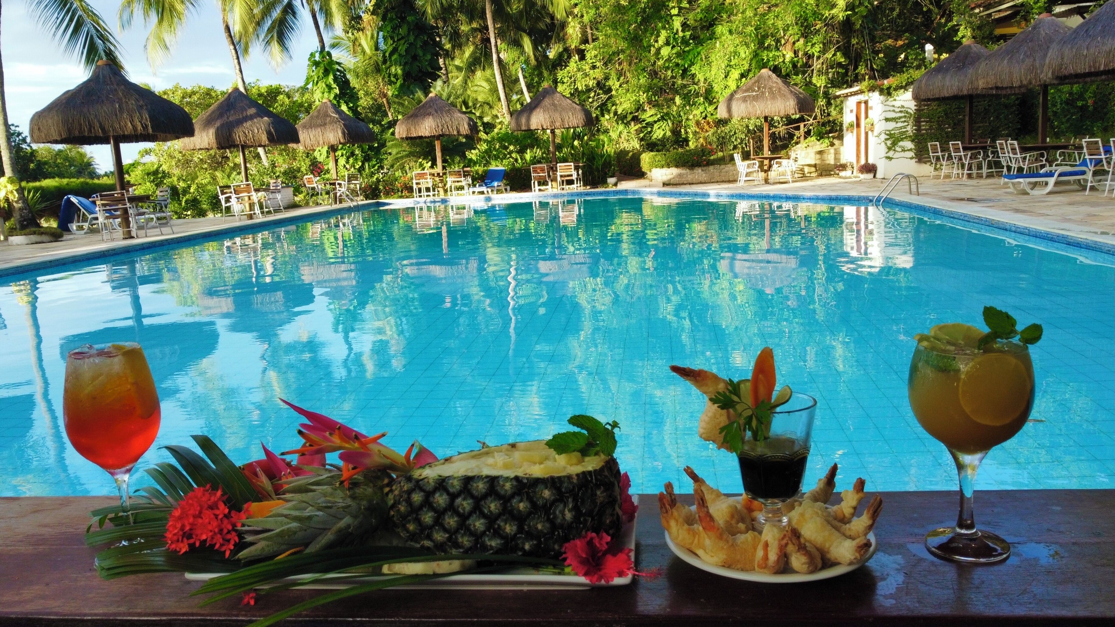 A poolside bar with a tropical setting, including a pool, lounge chairs, and thatched umbrellas.