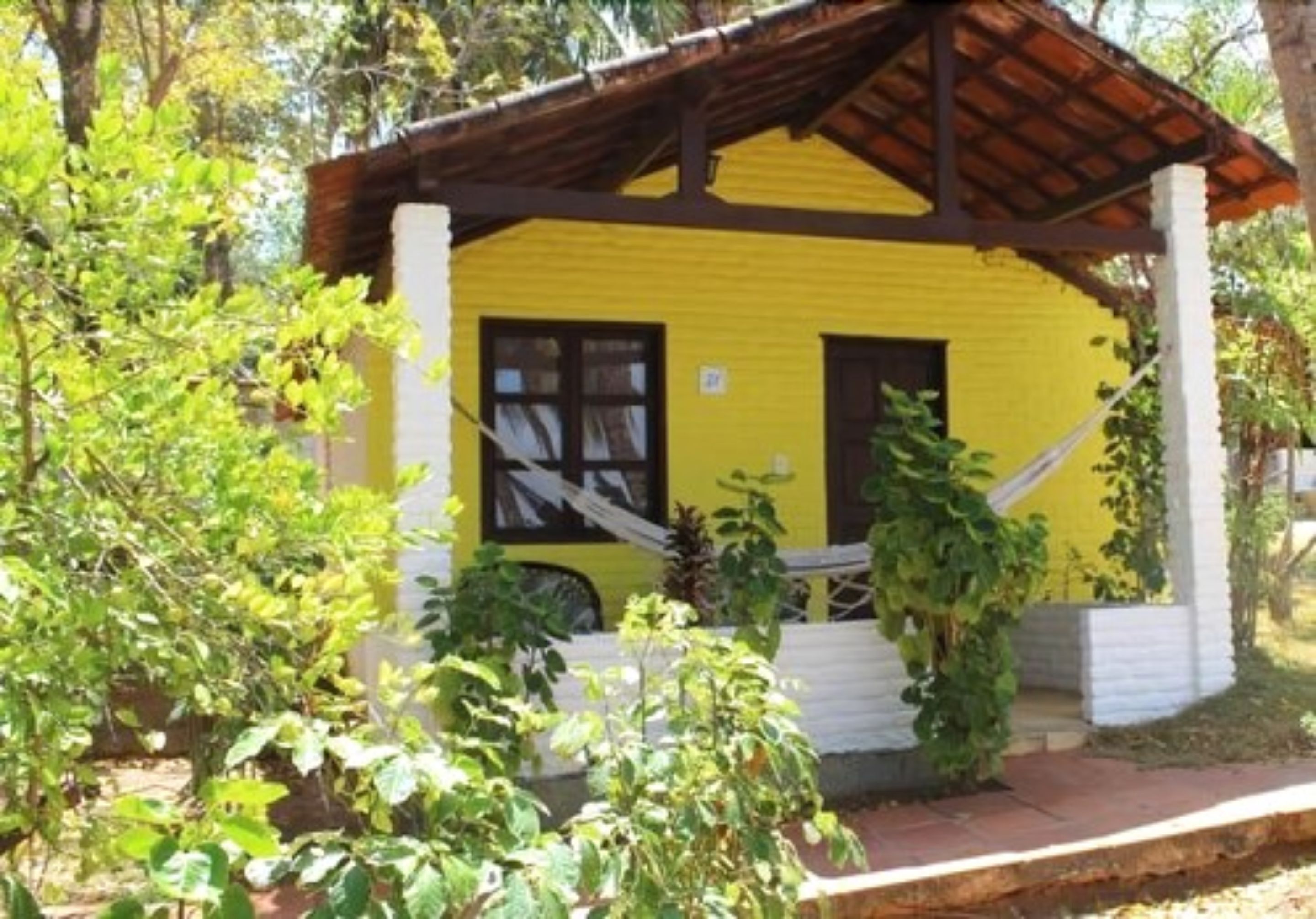 Un edificio amarillo con techo marrón, rodeado de vegetación.