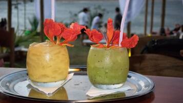 Dos bebidas sobre una bandeja, con vistas a un cuerpo de agua y personas al fondo.