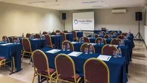 Un salón de conferencias con mesas, sillas, botellas de agua y una pantalla de proyector que muestra 'Planalto Bittar Hotel e Eventos'.