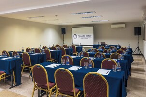 Un salón de conferencias con mesas, sillas, botellas de agua y una pantalla de proyector que muestra 'Planalto Bittar Hotel e Eventos'.