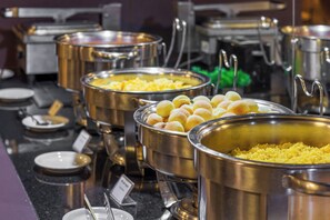 Servicio de comida tipo buffet con diferentes platos en recipientes metálicos.