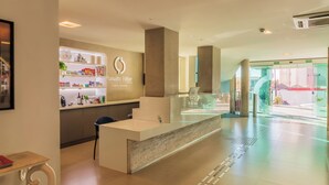 Zona de recepción de hotel con mostrador, área de descanso y puerta de cristal.