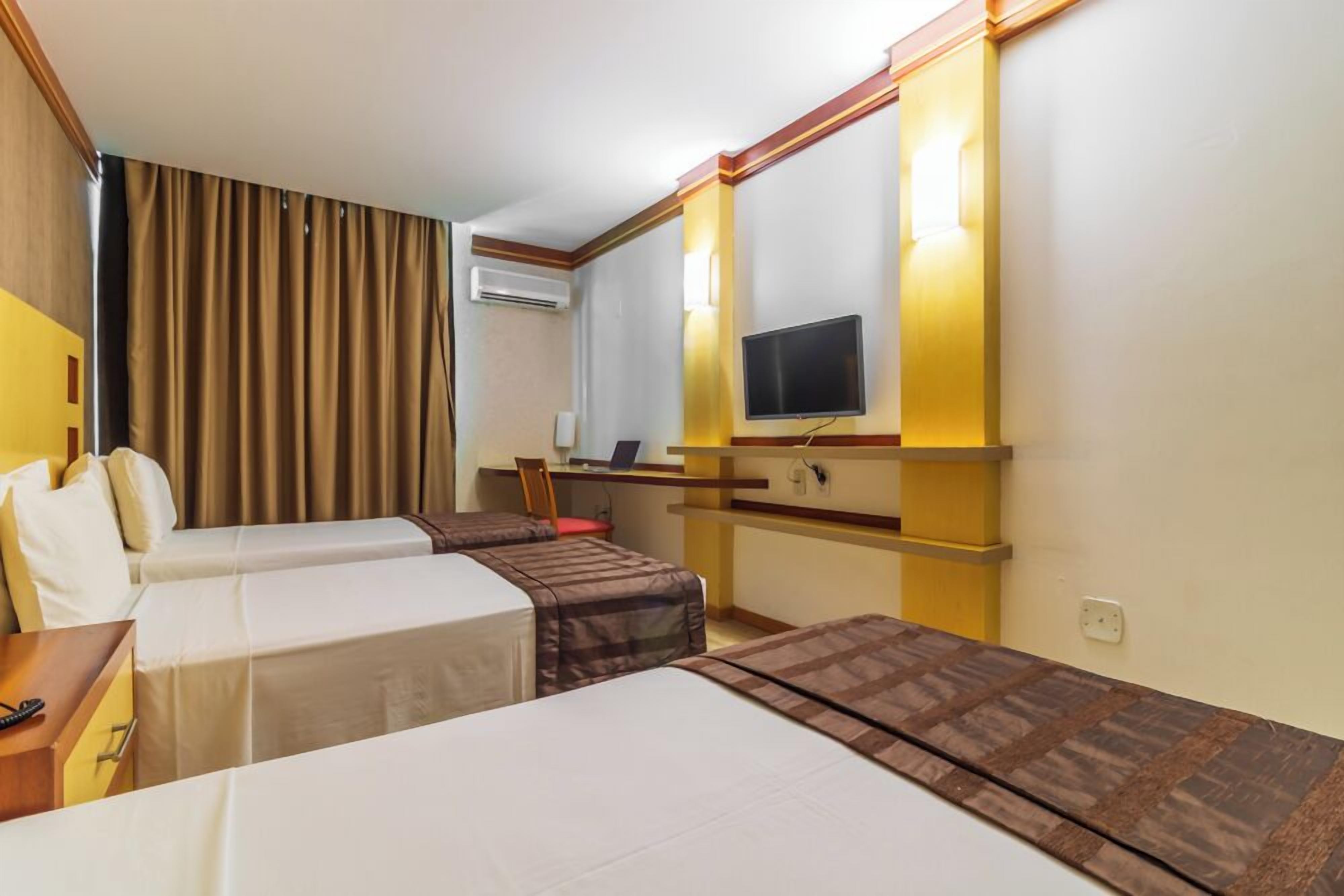 Una habitación de hotel con dos camas, un escritorio, una silla, un televisor y un equipo de aire acondicionado.
