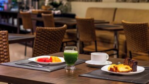 Una mesa de comedor con una porción de sandía, un vaso de jugo verde, una taza y una rebanada de pastel.