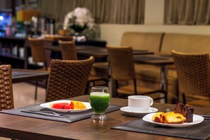Une table à manger avec une assiette de pastèque, un verre de jus vert, une tasse et une part de gâteau.