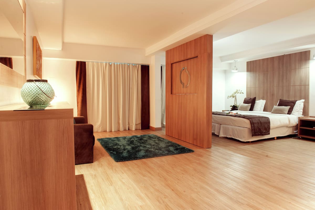 Ein modernes Schlafzimmer mit einem Holzschrank, einem Bett in Weißbraun und einem grünen Teppich auf Holzdielen.