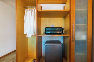 Una habitación compacta con un armario de madera, un refrigerador negro pequeño y una toalla blanca colgada en la puerta.