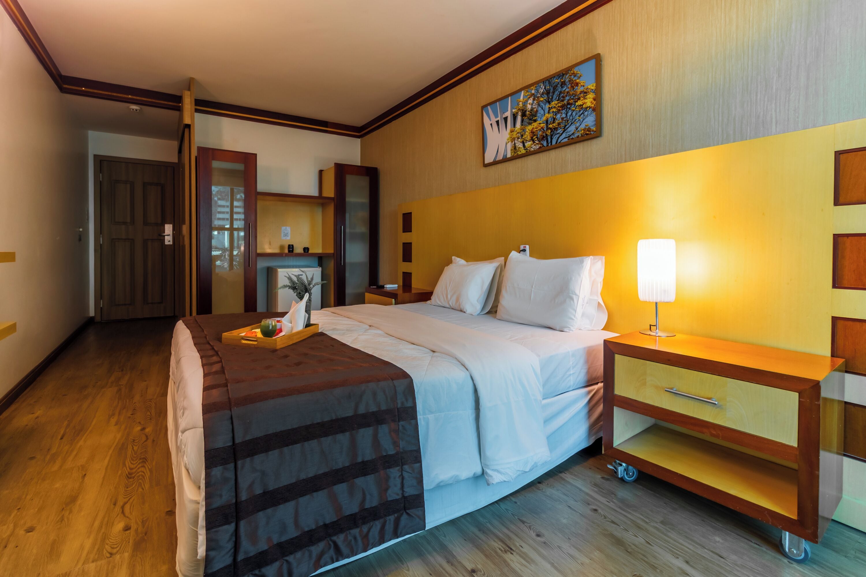 Een hotelkamer met een bed, nachtkastje, lamp en een houten vloer.